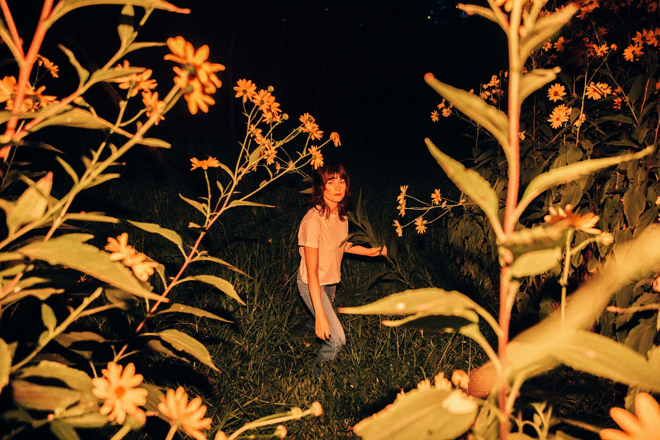A woman standing amidst a field of flowers under the night sky.