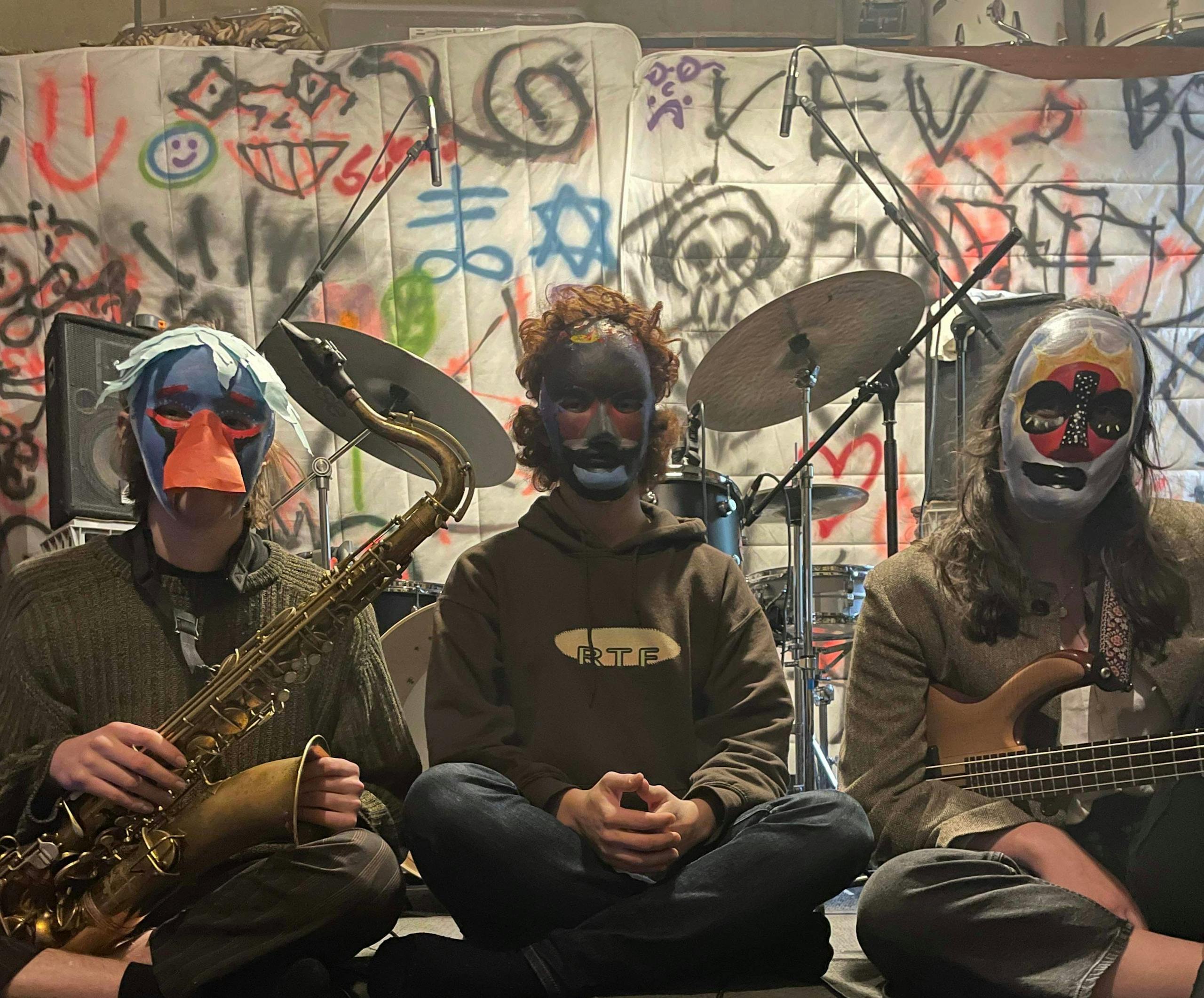 Three people wearing masks with graffiti behind them